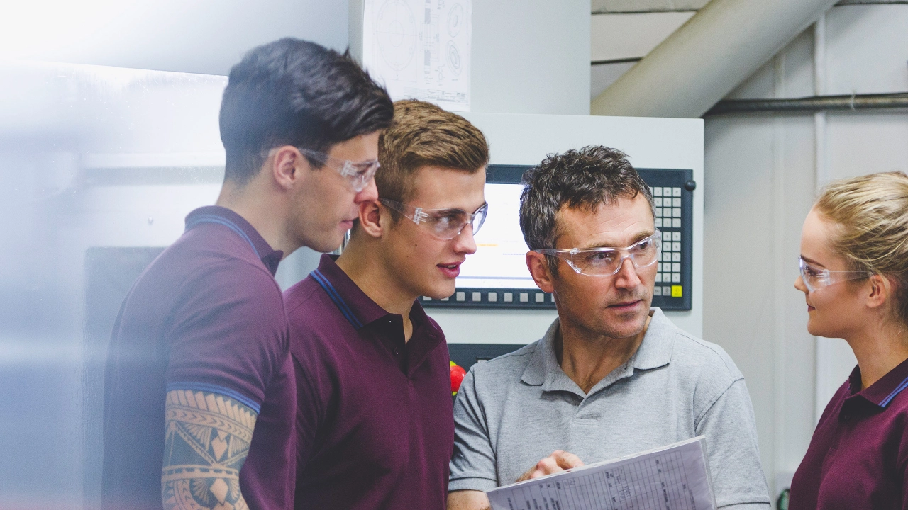 Ein Ausbilder steht mit drei Azubis zusammen und erklärt etwas.