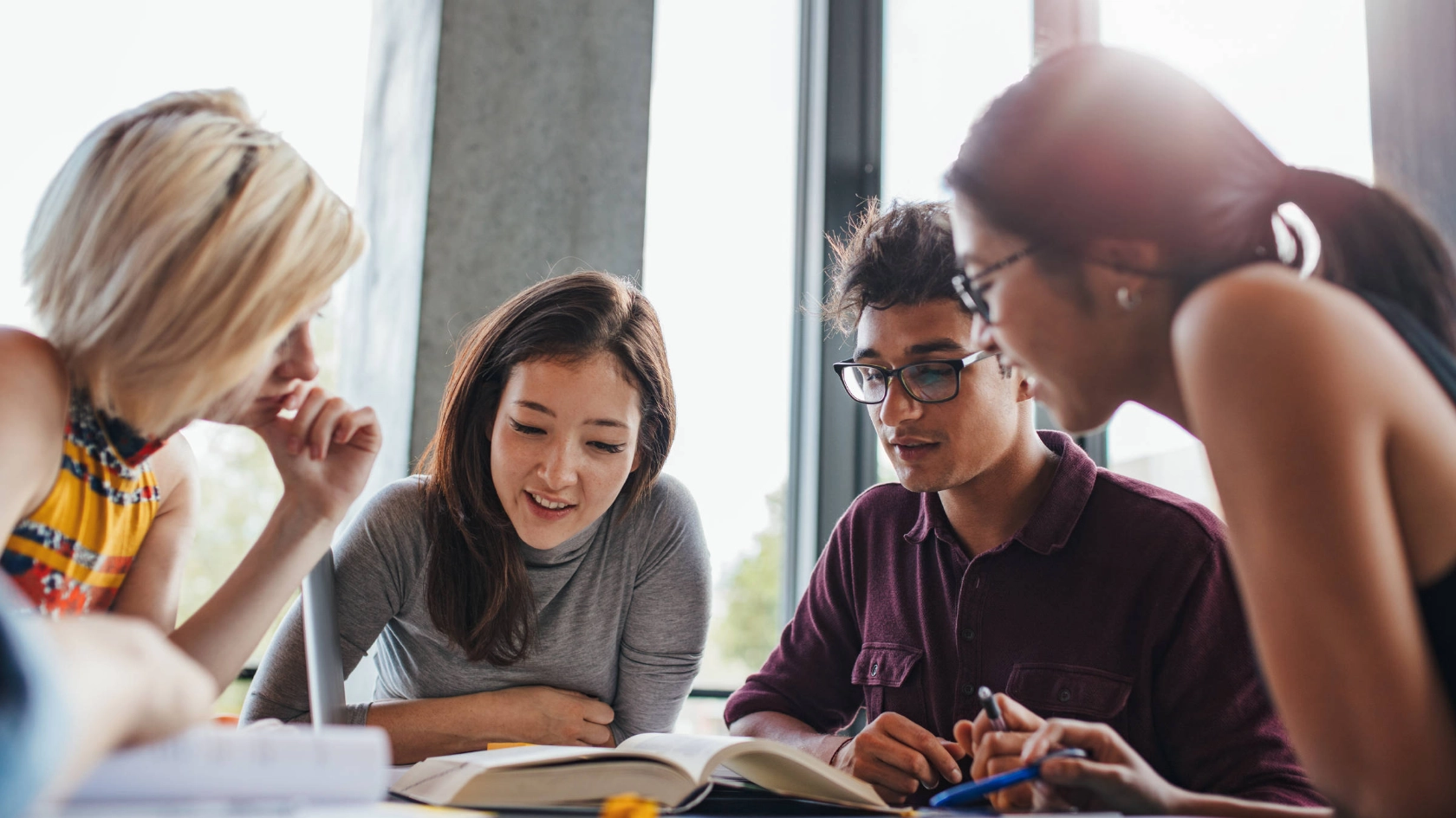 Vier Studierende blicken in Bücher, die vor ihnen auf dem Tisch liegen.