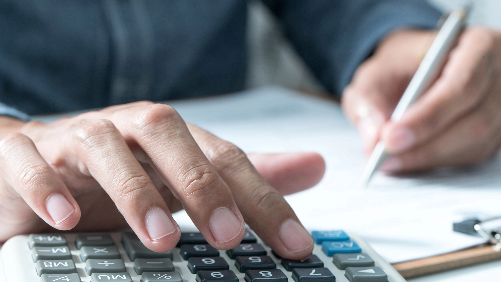 Ein Mann tippt auf einem Taschenrechner und macht dabei Notizen.