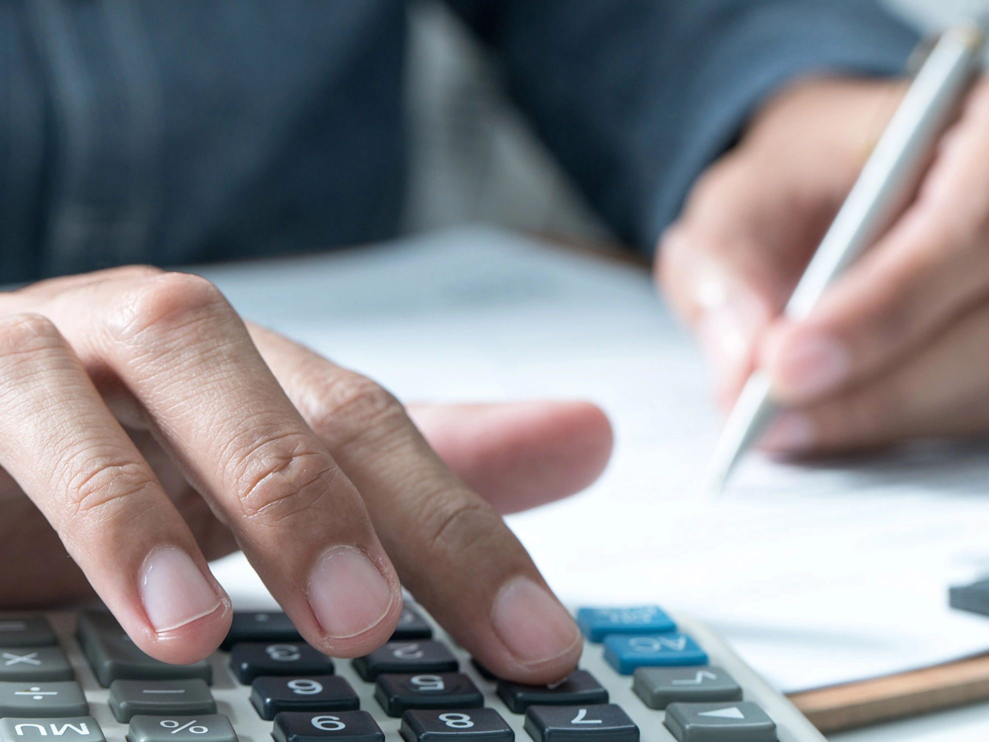 Ein Mann tippt auf einem Taschenrechner und macht dabei Notizen.