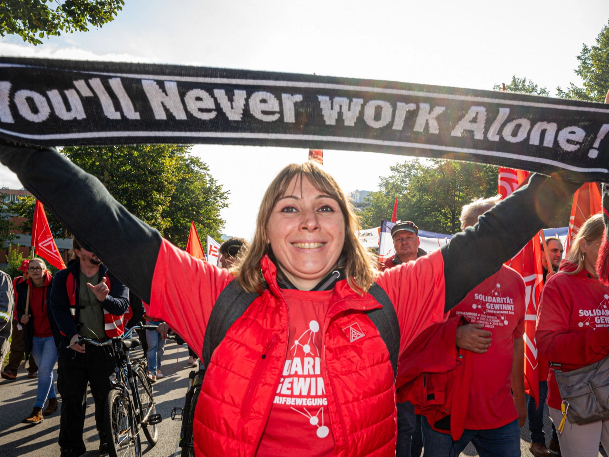 Eine Frau hält einen Schal hoch mit der Aufschrift „You never work alone“