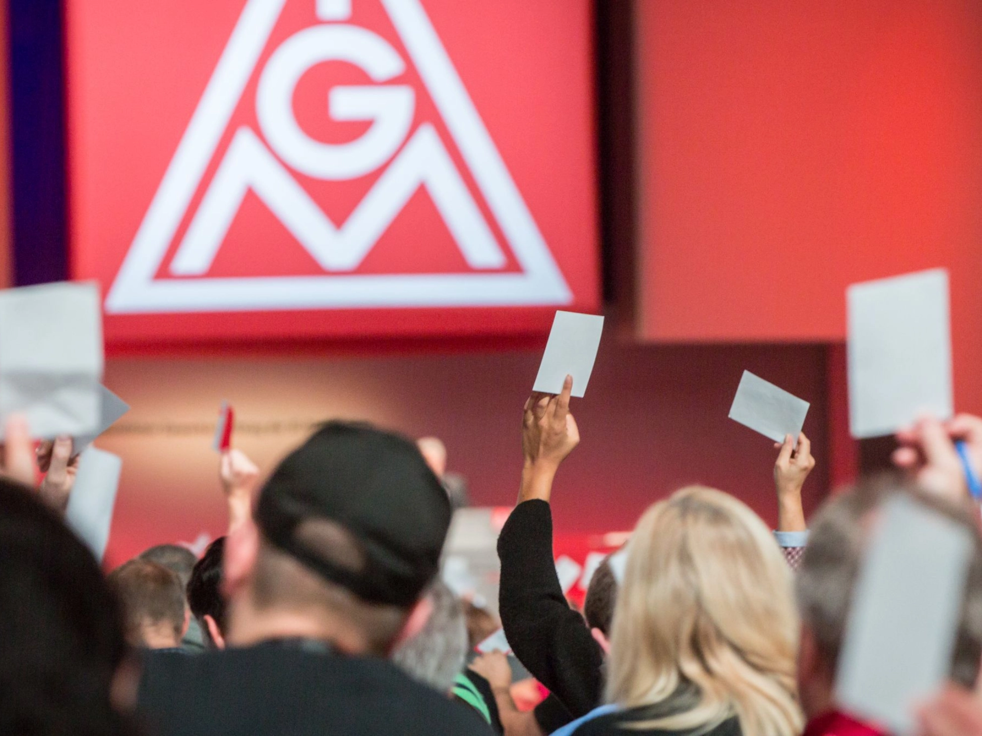 Delegierte auf dem Gewerkschaftstag 2015 der IG Metall bei einer Abstimmung, im Hintergrund das Logo der IG Metall